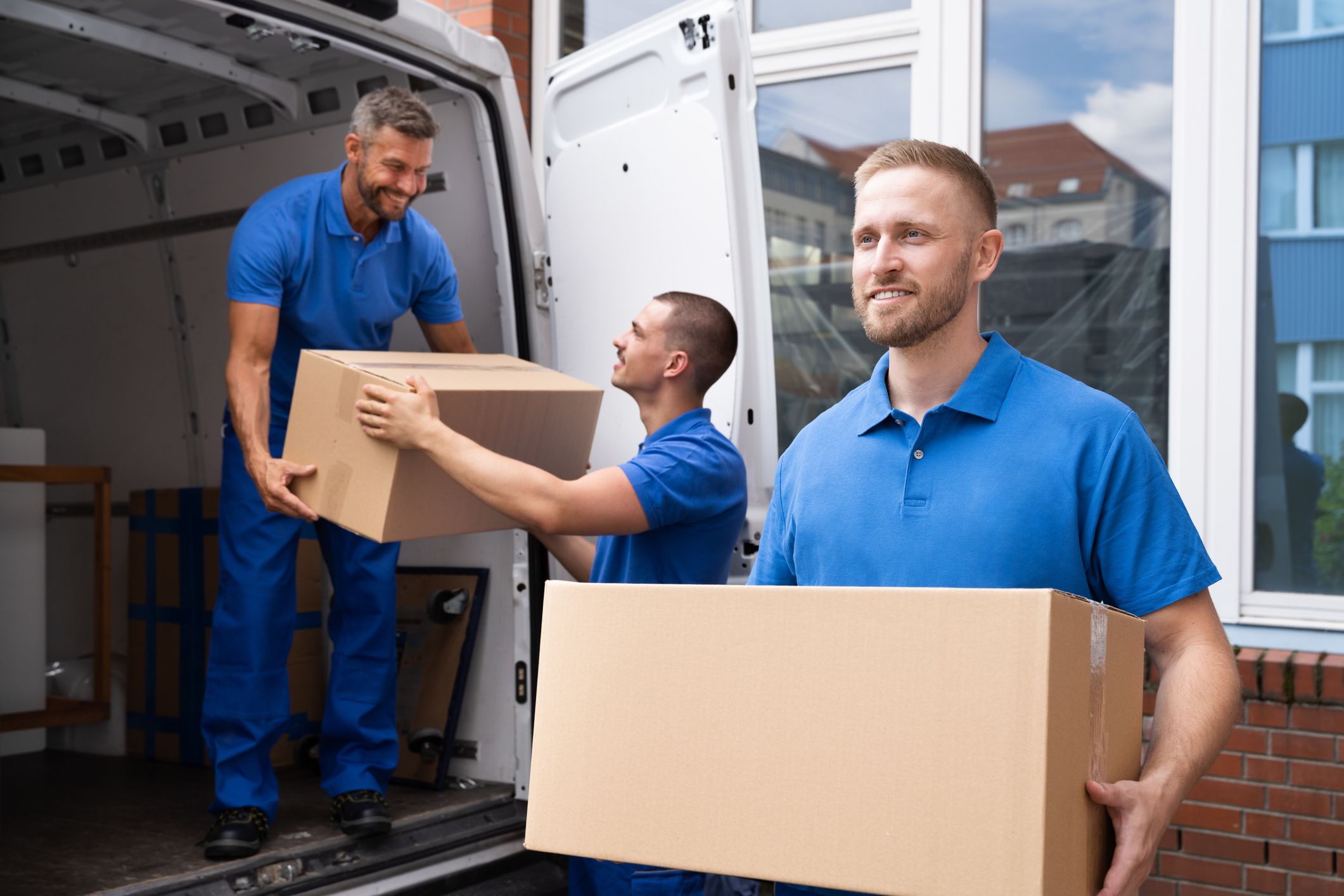 Umzugsteam lädt Umzugskartons aus Transporter vor Wohnhaus